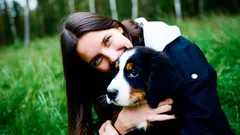 Mladá žena objímá psa na zelené trávě v přírodě, šťastný moment se zvířecím mazlíčkem